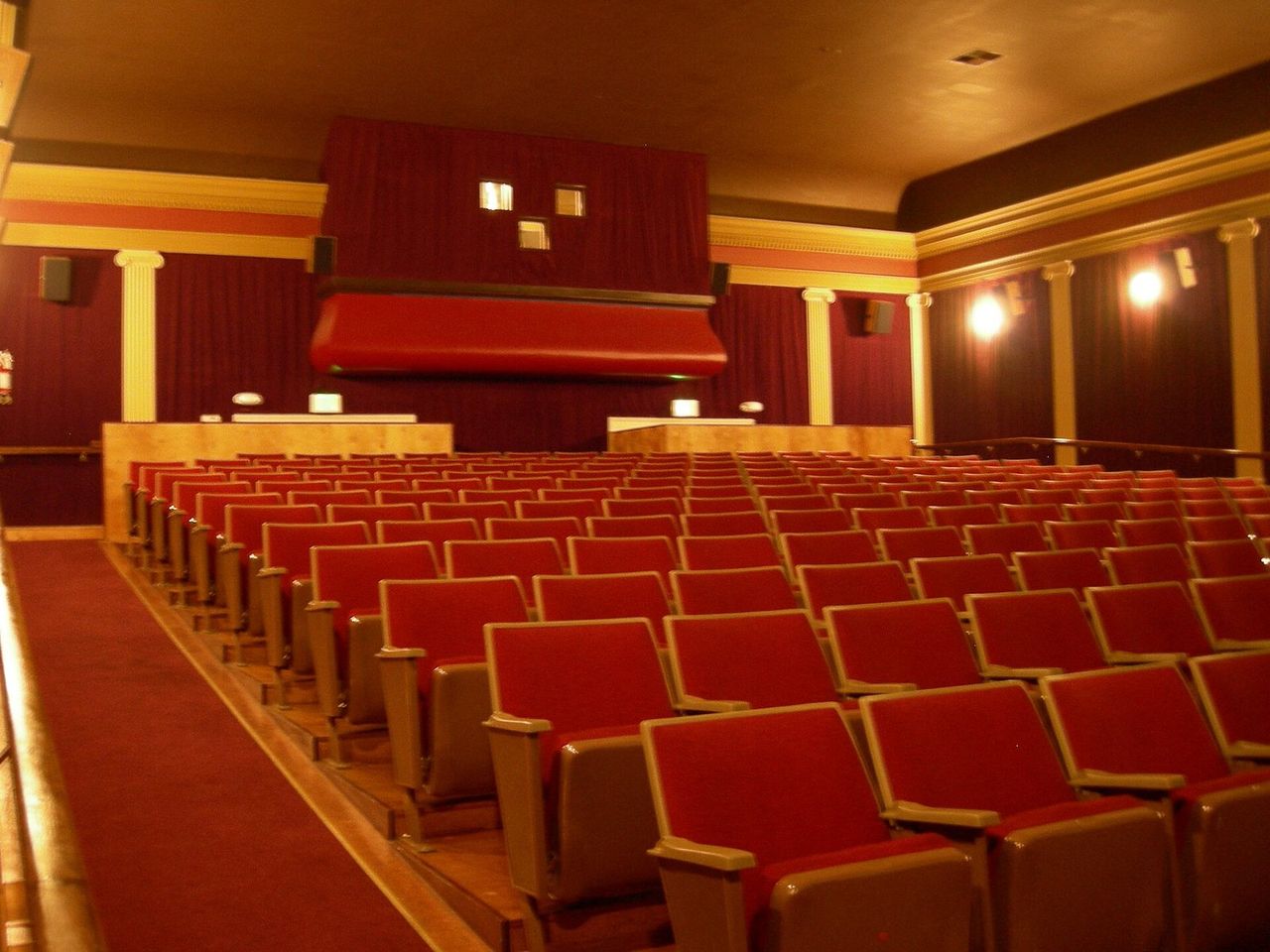 Empty commercial movie theater hall showing auditorium seating and projection screen Modern commercial cinema auditorium with rows of red velvet seats and large screen